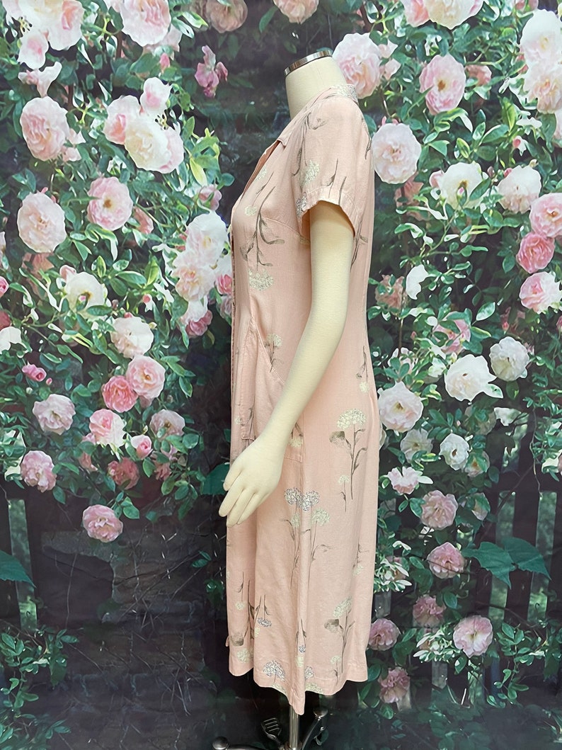 May include: A pink midi dress with a floral print. The dress has a V-neckline, short sleeves, and a button-up front.