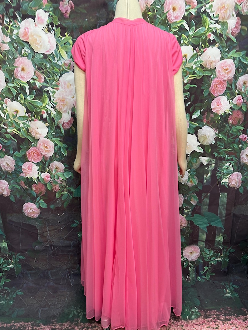 May include: A floor-length, bright pink nightgown featuring a solid-colored base layer with short sleeves and a sheer, flowing chiffon overlay that drapes from the shoulders to the hem, creating a layered, pleated appearance throughout the garment.