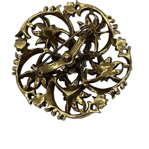 Pu&ograve; includere: Un fermaglio dorato con un design circolare che presenta intricati motivi floreali. Il fermaglio ha una chiusura a spilla e gancio sul retro.