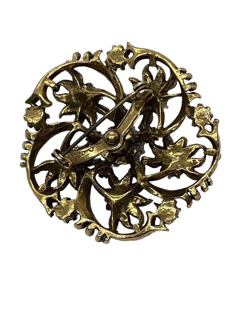 Pu&ograve; includere: Un fermaglio dorato con un design circolare che presenta intricati motivi floreali. Il fermaglio ha una chiusura a spilla e gancio sul retro.