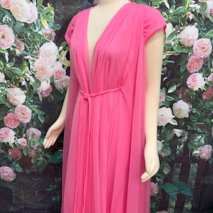 May include: A floor-length hot pink gown featuring a deep V-neckline, short cap sleeves, and a sheer chiffon overlay. The dress includes a matching thin fabric tie belt at the waist that creates vertical pleats and a flowing silhouette.