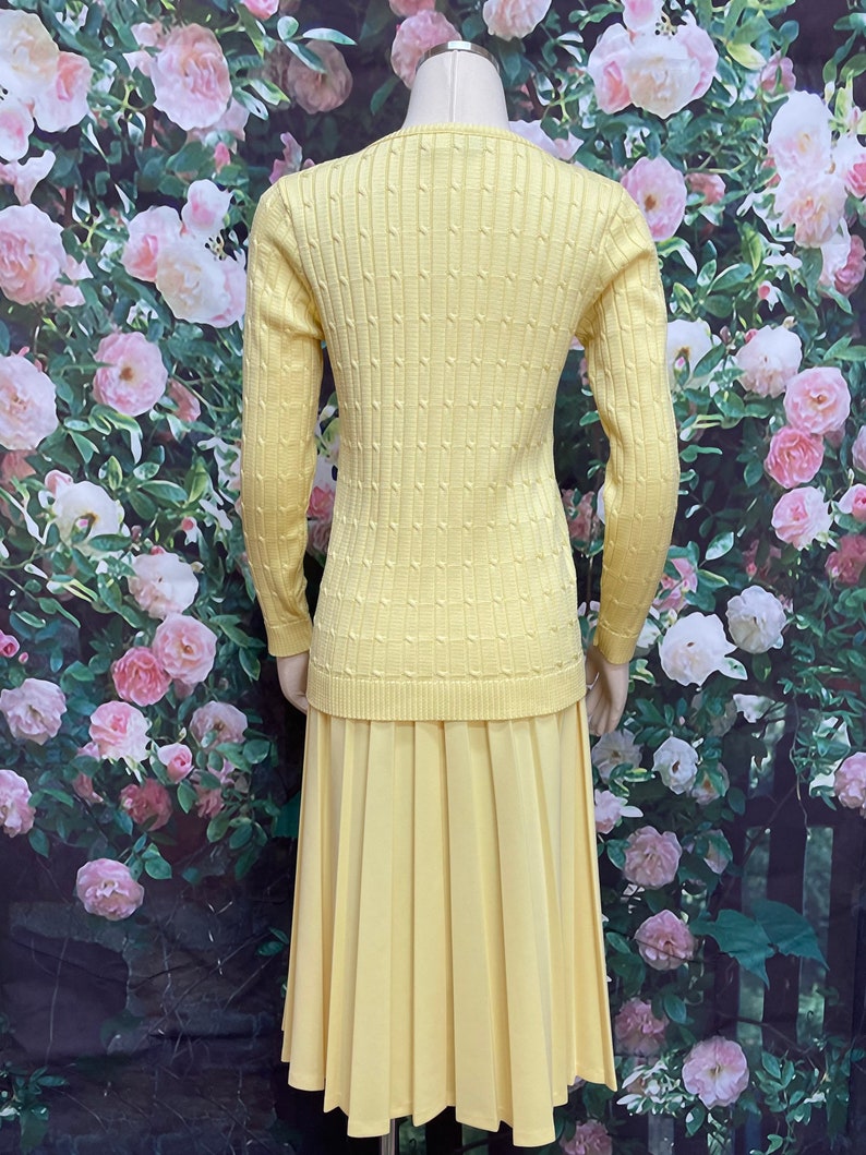 May include: A yellow knitted sweater and matching pleated skirt set. The sweater has a cable knit pattern and long sleeves. The skirt is knee-length and has a smooth texture.