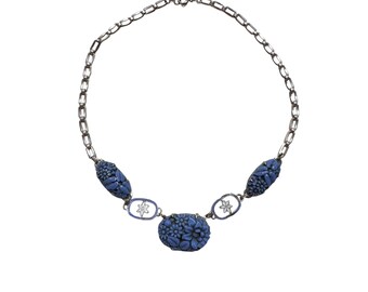 May include: A silver chain necklace with three blue floral-shaped pendants. The pendants are carved with intricate floral designs.