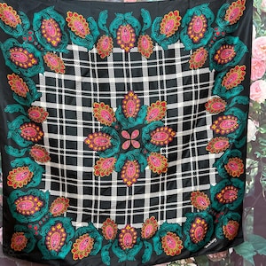 May include: A black and white plaid square scarf with a teal, pink, and yellow floral design around the border.