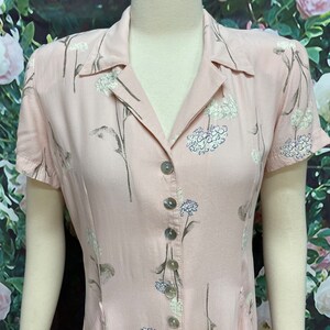 May include: A pink button-down dress with a floral print. The dress has short sleeves and a collared neckline.