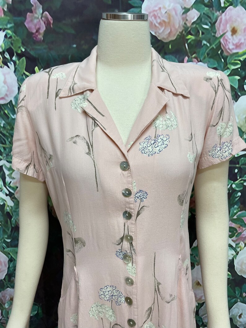 May include: A pink button-down dress with a floral print. The dress has short sleeves and a collared neckline.
