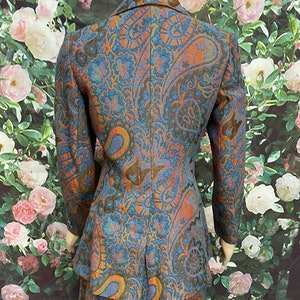 May include: A blue, orange and gold paisley patterned blazer and skirt set. The blazer has a notched collar and long sleeves. The skirt is A-line and falls to the knee.