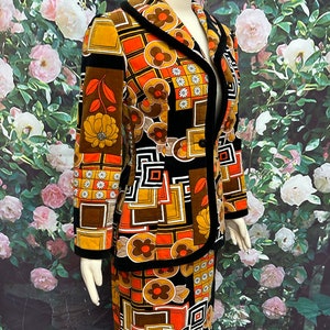 May include: A vintage two-piece suit with a geometric and floral pattern in shades of brown, orange, and black. The jacket has a black velvet collar and trim. The skirt is a-line and has a black velvet waistband.