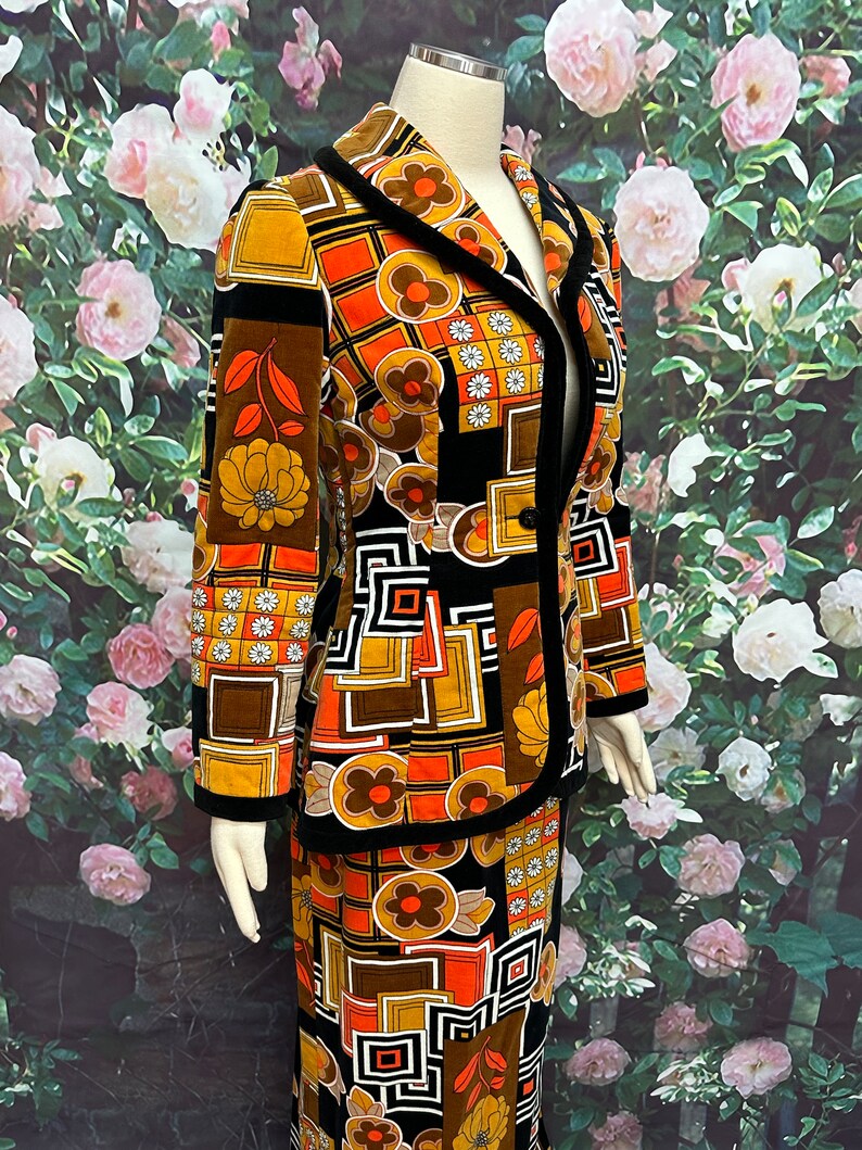 May include: A vintage two-piece suit with a geometric and floral pattern in shades of brown, orange, and black. The jacket has a black velvet collar and trim. The skirt is a-line and has a black velvet waistband.