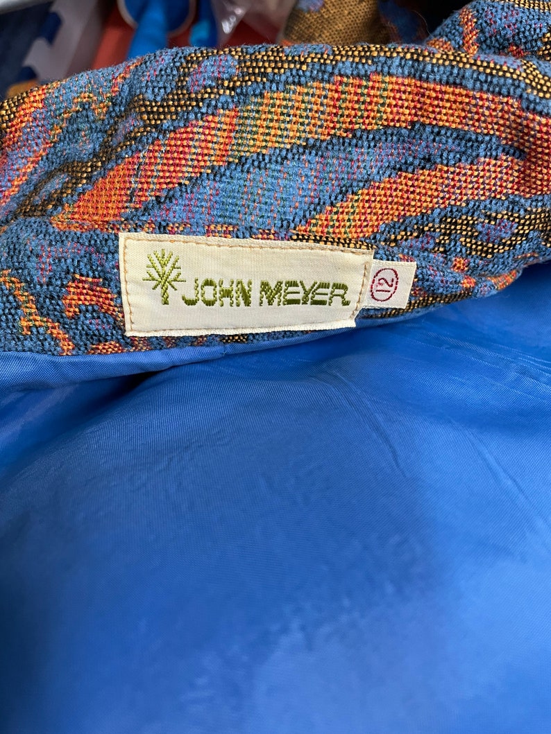 May include: A close-up of a blue and orange patterned fabric with a white tag that reads "JOHN MEYER" and a size 12 tag.