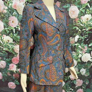 May include: A blue and orange paisley patterned skirt suit. The jacket has a notched collar and a single button closure. The skirt is knee-length.