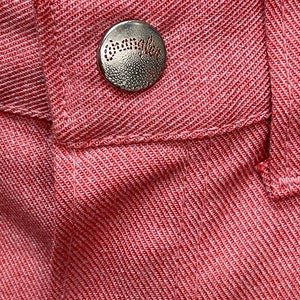 May include: Close-up of a red fabric with a silver button that says " Wrangler" on it.