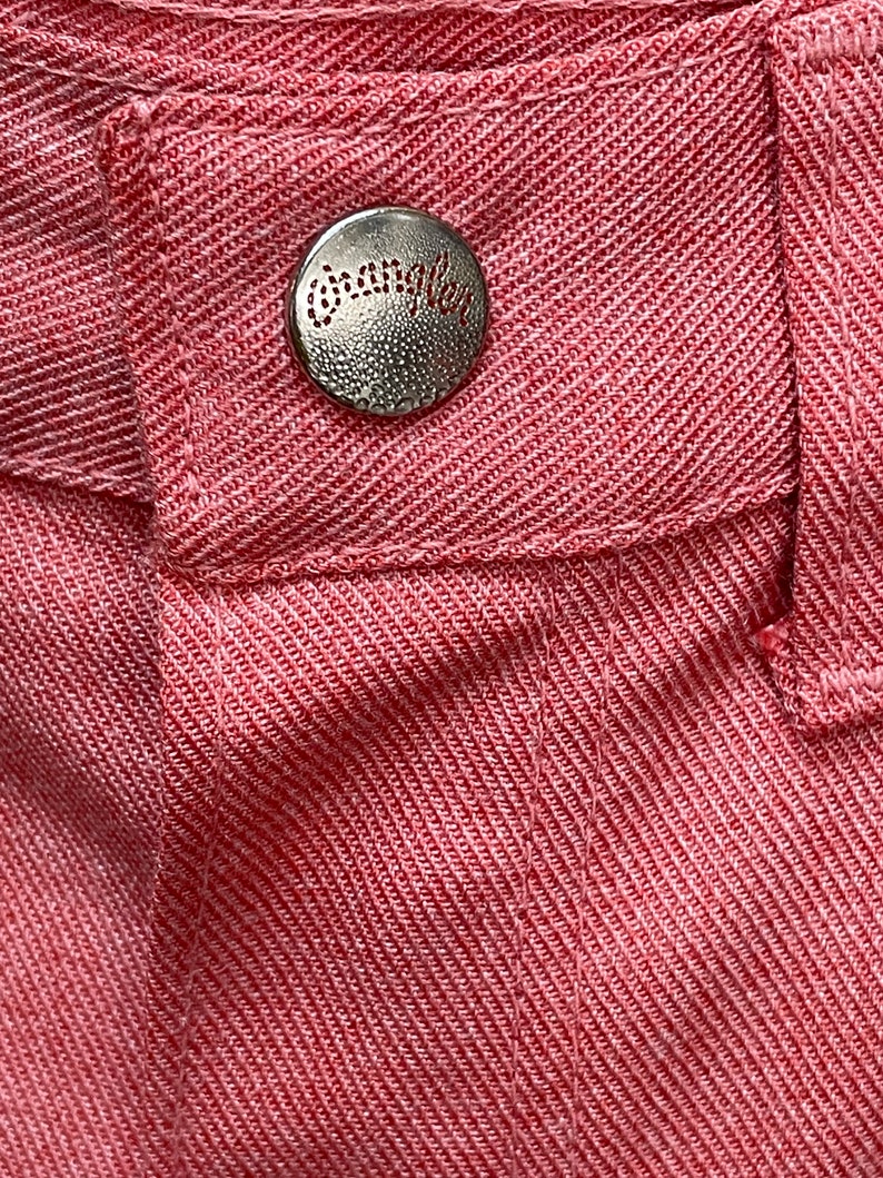 May include: Close-up of a red fabric with a silver button that says " Wrangler" on it.