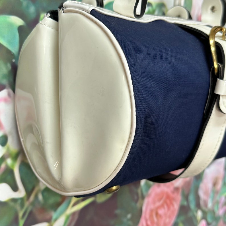 May include: A white and navy blue cylindrical handbag with a white leather strap and a gold buckle.