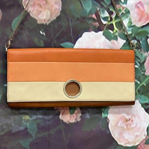 May include: A striped orange, peach and cream leather clutch with a silver ring detail. The clutch has a gold chain strap.