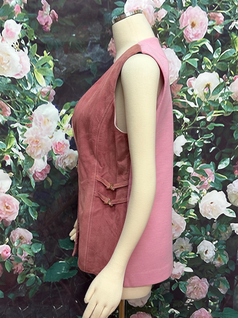 May include: A sleeveless vest with a pink and rose-colored design. The vest has a button closure and a decorative strap detail on the front.
