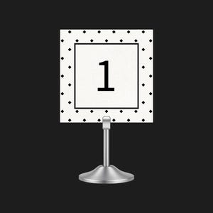 May include: A table number card featuring the number 1 in black on a white background. The card has a black border and is decorated with black diamond shapes. It is held by a silver metal stand, suitable for events or celebrations.