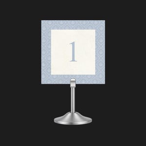 May include: A table number card on a silver stand. The card features the number 1 in light blue on a white background, framed by a light blue patterned border. Ideal for weddings or events.