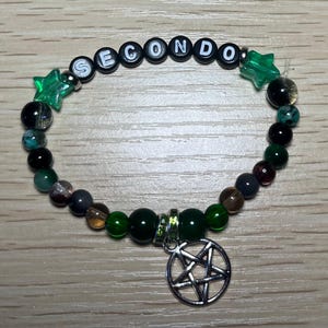 May include: A beaded bracelet with the word "SECONDO" spelled out in black and white letter beads. The bracelet features green star-shaped beads, various colored round beads, and a silver pentagram charm. The beads are in shades of green, brown, and black.