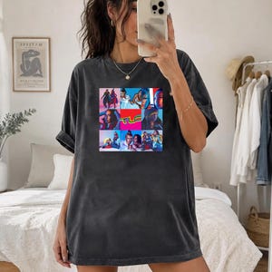 May include: A charcoal grey oversized t-shirt featuring a square graphic print on the chest. The print contains a collage of nine colourful images of the music group TLC, with the bright yellow and green TLC logo centred in the middle of the grid.