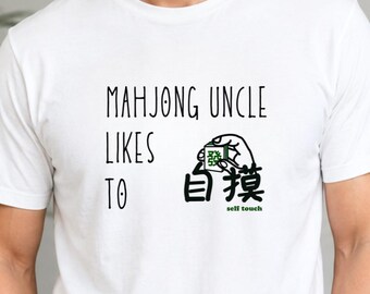 May include: A white short-sleeved t-shirt featuring the black text "MAHJONG UNCLE LIKES TO" followed by a graphic of a hand holding a green mahjong tile and the black Chinese characters "自摸" with the green text "self touch" underneath.