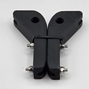 May include: Black metal bracket with two angled arms, each with a circular hole. The arms are connected by two vertical pieces, secured with bolts and nuts. A black zip tie holds the pieces together.