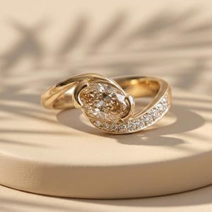 May include: A gold ring featuring a central oval-shaped champagne-colored gemstone held in a bypass setting, with a band accented by a row of small, clear, round-cut stones along one side of the shank, creating a polished and reflective appearance.