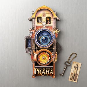 Pode incluir: Um relógio decorativo de madeira com um design detalhado, com um mostrador azul, figuras e a palavra "PRAHA". Inclui uma chave e um pequeno cartão com uma ilustração de um edifício. O relógio tem cerca de 25 cm de altura.