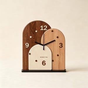 Peut inclure: Une horloge en bois au design arqué unique. Elle présente des tons marron foncé, marron clair et crème. Les chiffres 12, 9, 6 et 3 sont visibles. Les aiguilles sont noires. Le socle est noir. Le texte "ONE MOMENT'S TIME" est visible.