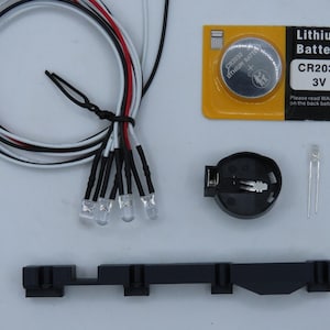 May include: A collection of electronic components, including a CR2032 3V lithium battery, LED lights, a battery holder, and a black plastic mounting bracket. Wires are black, white, and red.