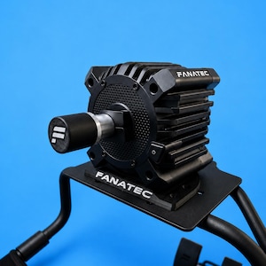 Op de afbeelding: Een zwarte Fanatec racestuur-basis met een getextureerde ronde voorplaat, een centrale as met een zwarte dop voorzien van een wit logo en een aan-uitknop aan de zijkant. De unit is gemonteerd op een zwarte metalen beugel met de merknaam Fanatec.