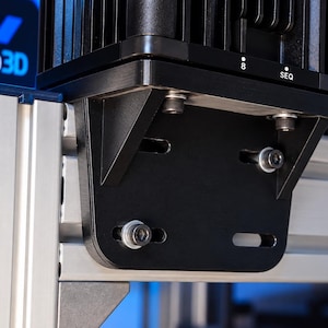 May include: A black metal mounting bracket attached to a silver aluminum extrusion frame. The bracket features horizontal slots and is secured with silver bolts. A black electronic component with the text 8 and SEQ is mounted above the bracket.