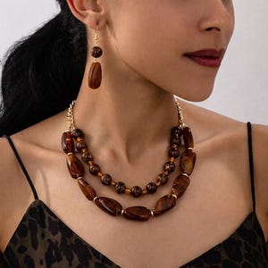 Peut inclure: Un ensemble de collier et boucles d'oreilles assorties. Le collier présente de grosses perles ovales marron et de plus petites perles rondes, reliées par une chaîne dorée. Les boucles d'oreilles ont un design similaire, avec une perle ronde et une longue perle ovale.