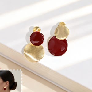 Peut inclure: Une paire de boucles d'oreilles composées de deux disques circulaires chacune. Un disque est en métal doré brossé et l'autre est en émail rouge profond lisse. Les boucles d'oreilles présentent un petit disque supérieur et un disque inférieur plus grand.