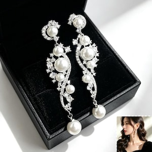 May include: A pair of long, silver-toned drop earrings featuring a curved, vine-like design encrusted with clear, sparkling crystals and multiple round, white faux pearls of varying sizes, with a single pearl drop at the bottom of each.