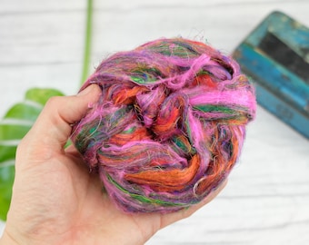 May include: A close-up of a ball of colorful recycled sari silk fibers in shades of pink, orange, green, and purple. The fibers are soft and fluffy, and they are perfect for crafting.