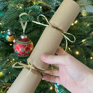 May include: A brown paper Christmas cracker tied with a natural twine bow. The cracker is decorated with a gold ribbon.