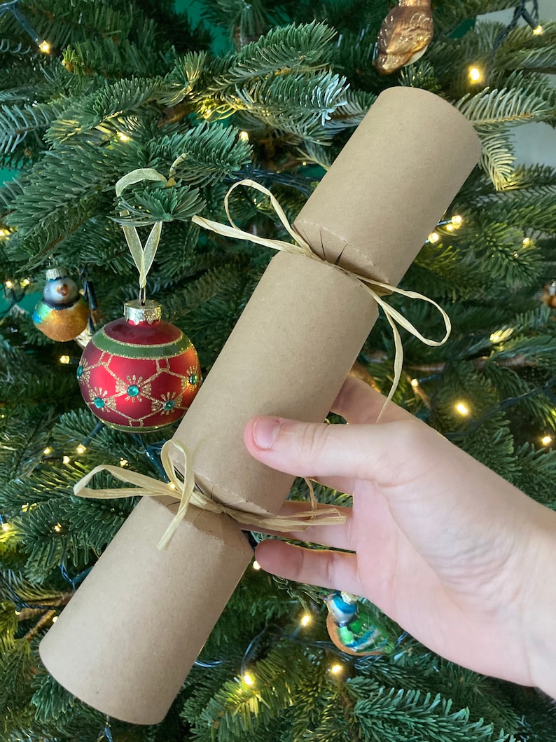 May include: A brown paper Christmas cracker tied with a natural twine bow. The cracker is decorated with a gold ribbon.
