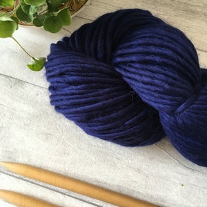 Puede incluir: Un ovillo de lana azul oscuro con dos agujas de tejer de madera.