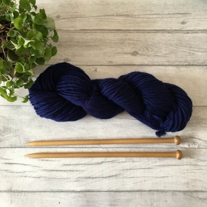 Puede incluir: Un ovillo de lana azul marino con dos agujas de tejer de madera.