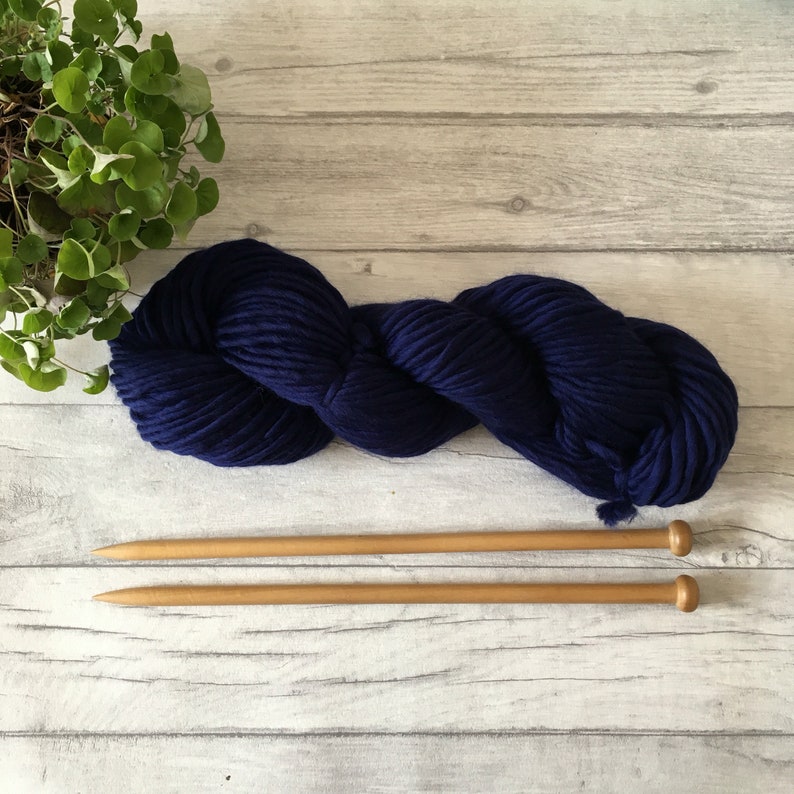 Puede incluir: Un ovillo de lana azul marino con dos agujas de tejer de madera.