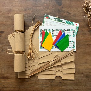 Christmas Cracker Kit. The photo shows a made up Christmas cracker which you can make with the kit plus everything the kit contains. Premium hats, jokes and instructions on a festive design background, snaps and raffia