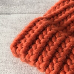 Puede incluir: Primer plano de una tela de punto grueso de color naranja quemado. La tela est&aacute; hecha de hilo grueso y tiene una textura suave y peluda.