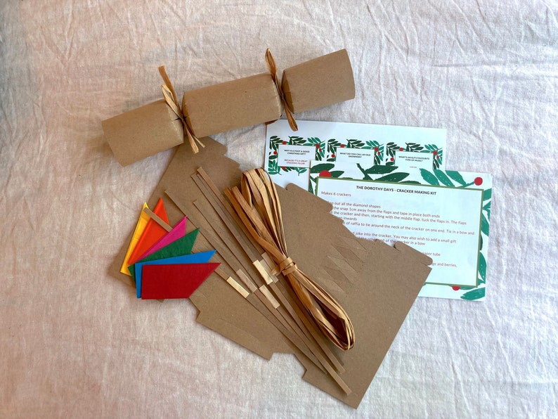 May include: A DIY Christmas cracker making kit with brown paper tubes, colorful paper flags, and instructions on how to make the crackers. The kit includes the text "The Dorothy Days Cracker Making Kit".