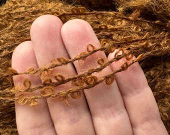 Könnte beinhalten: Nahaufnahme eines braunen Garns mit flauschigem Charakter. Das Garn wird in einer Hand gehalten und zeigt die geschlungene Textur.