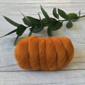 Peut inclure: Gros plan d'une laine card&eacute;e orange vif, un type de fibre utilis&eacute;e pour le feutrage et le filage, dispos&eacute;e en spirale. La laine card&eacute;e est sur une surface en bois gris clair.