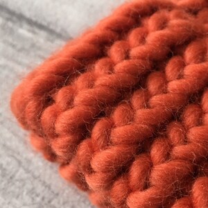 Puede incluir: Primer plano de una tela de punto grueso de color naranja quemado. La tela est&aacute; hecha de hilo grueso y tiene una textura suave y peluda.