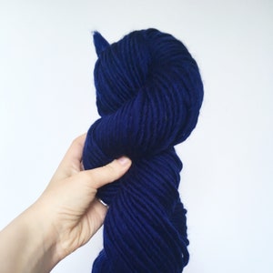 Puede incluir: Un ovillo de hilo azul oscuro, sostenido en una mano, listo para tejer o hacer ganchillo.