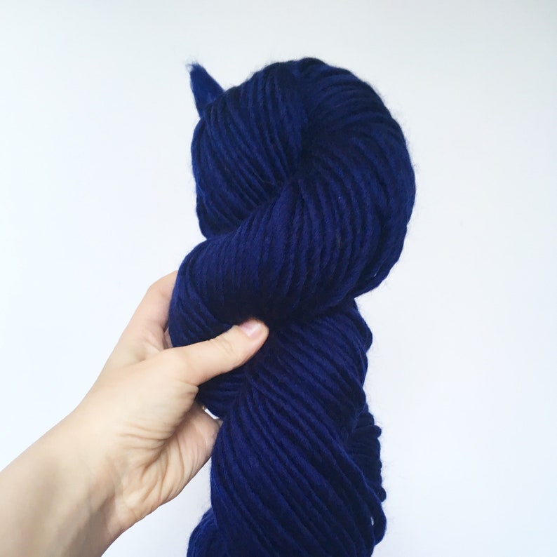 Puede incluir: Un ovillo de hilo azul oscuro, sostenido en una mano, listo para tejer o hacer ganchillo.