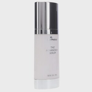 May include: A cylindrical SkinMedica TNS ADVANCED+ SERUM bottle with a metallic silver cap and base. The white opaque container features black text reading SkinMedica, TNS ADVANCED+ SERUM, and NET WT. 1.0 OZ / 28.4 G printed on the front surface.